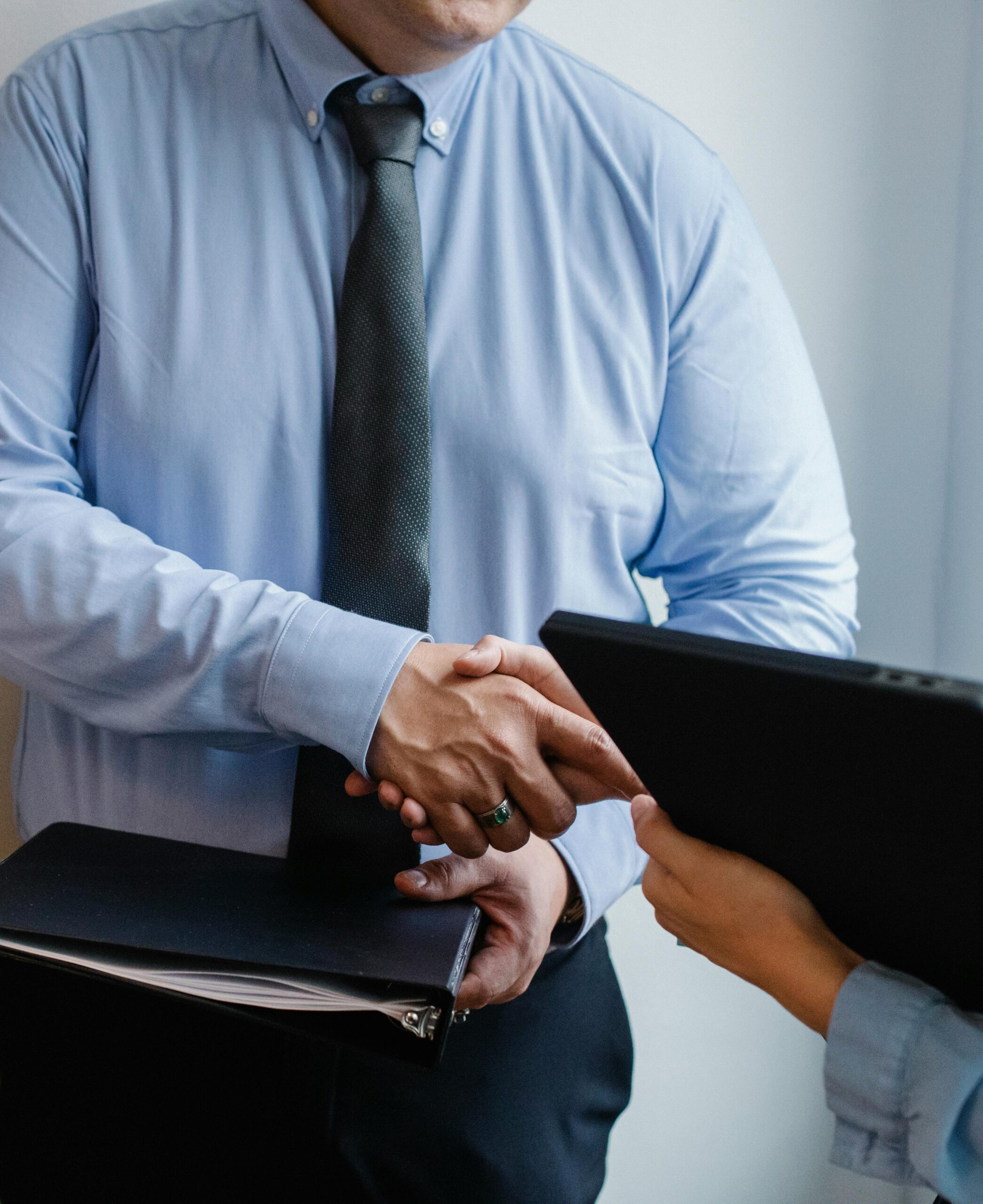 Faceless coworkers in formal clothes shaking hands during meeting at work in light office